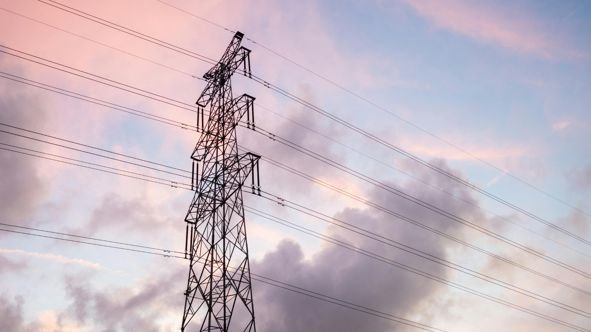 Pylône électrique haute tension et ses lignes sous un ciel rosé et nuageux