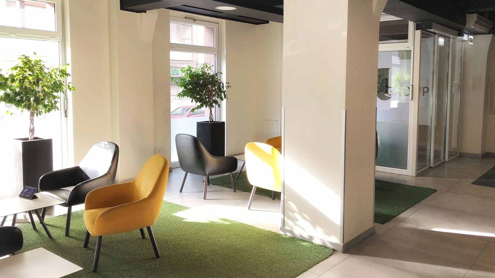Espace lounge d'entreprise lumineux avec fauteuils jaunes et noirs, plantes vertes et large baie vitrée apportant un éclairage naturel