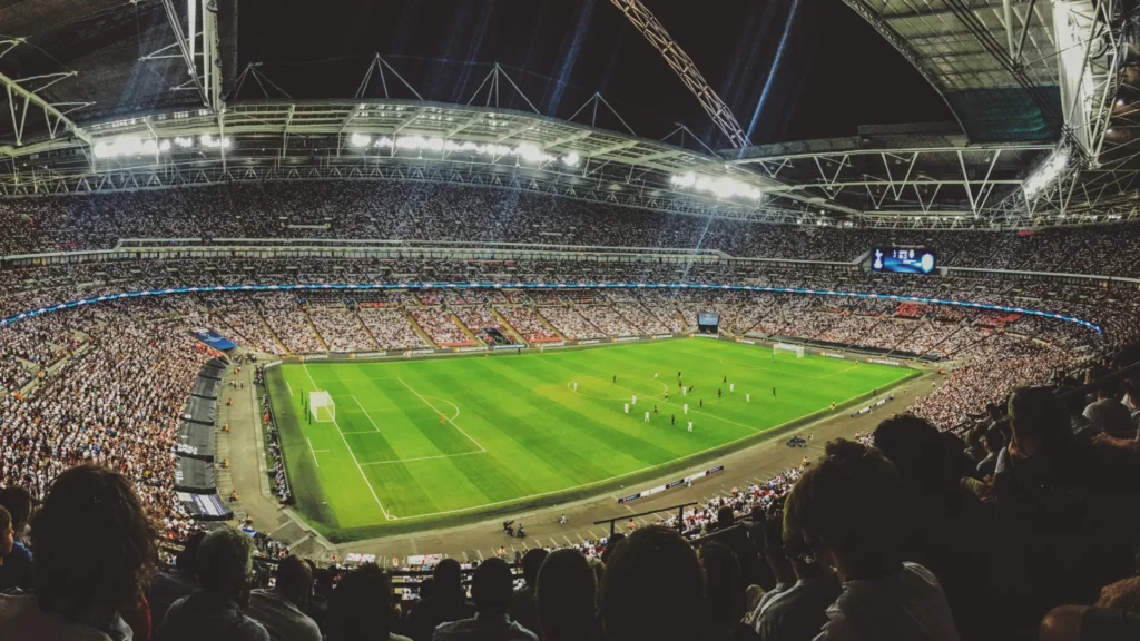 Stade de football rempli de spectateurs lors d’un match en soirée, illustrant l’énergie d’un grand événement sportif.
