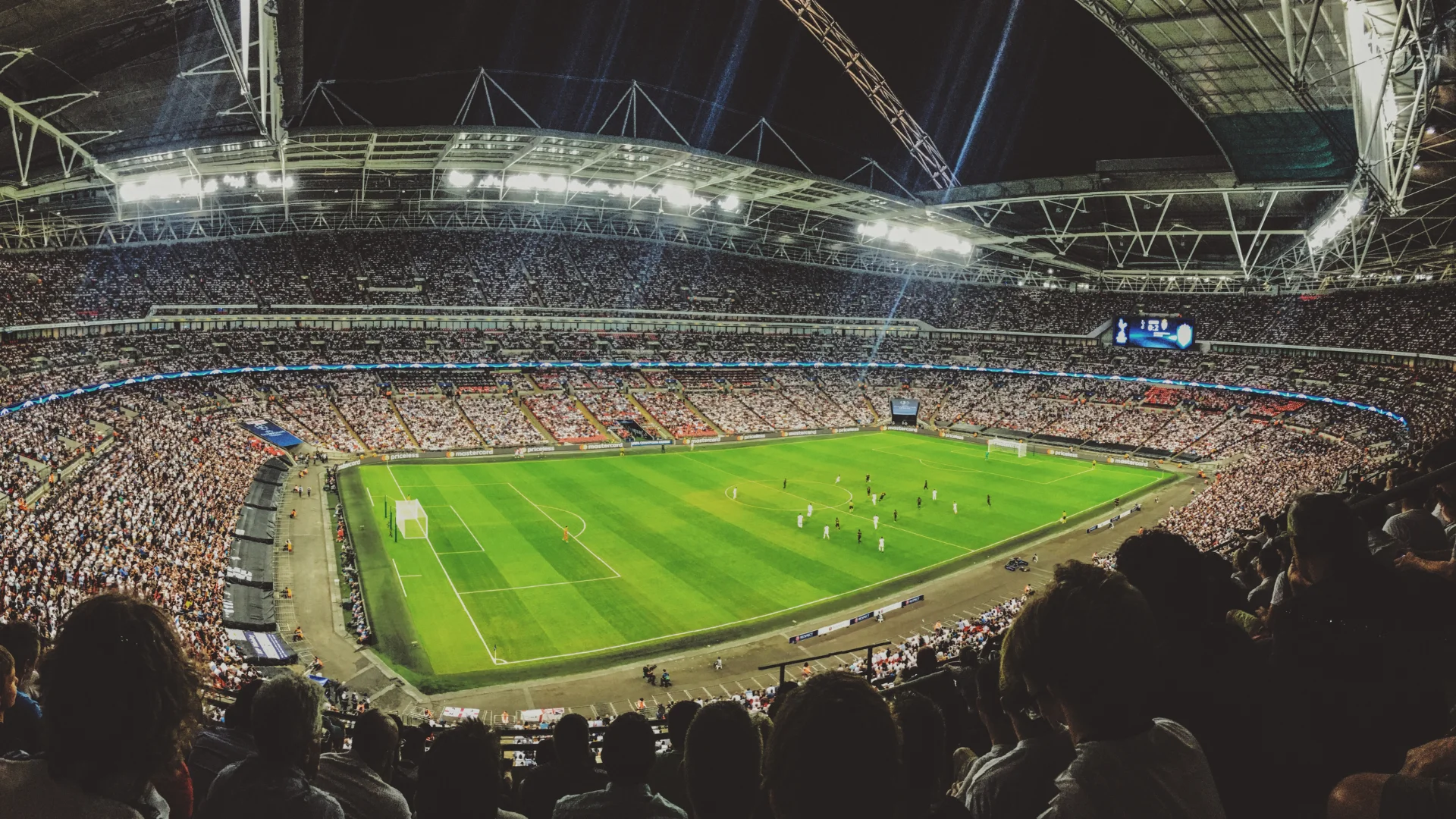Stade de football rempli de spectateurs lors d’un match en soirée, illustrant l’énergie d’un grand événement sportif.