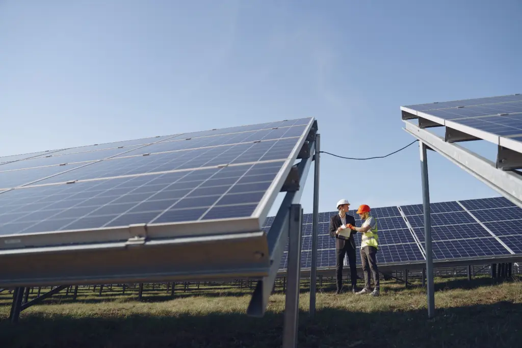 Deux professionnels en tenue de chantier échangeant devant des panneaux solaires photovoltaïques dans un champ, énergie renouvelable en entreprise