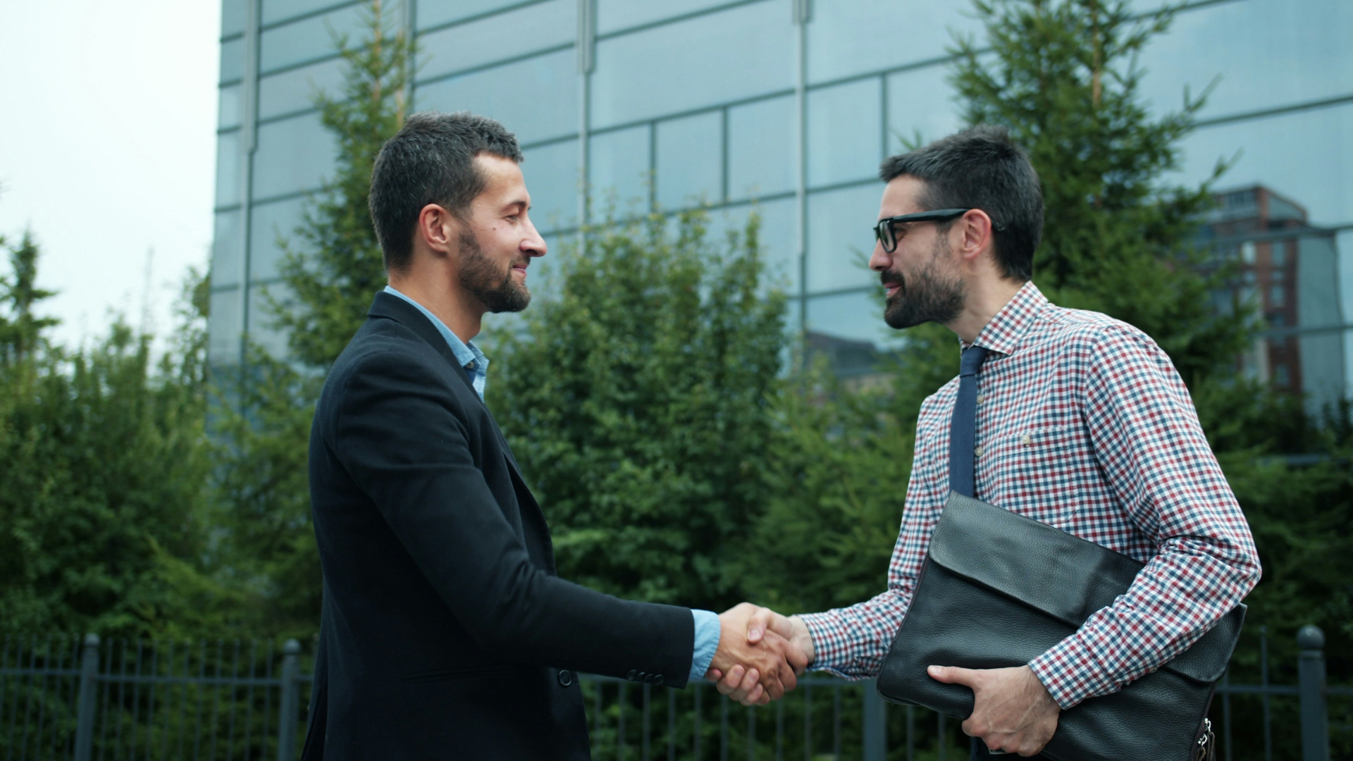 Poignée de main entre deux professionnels devant un immeuble de bureaux, illustrant le rachat d'un fournisseur d'électricité