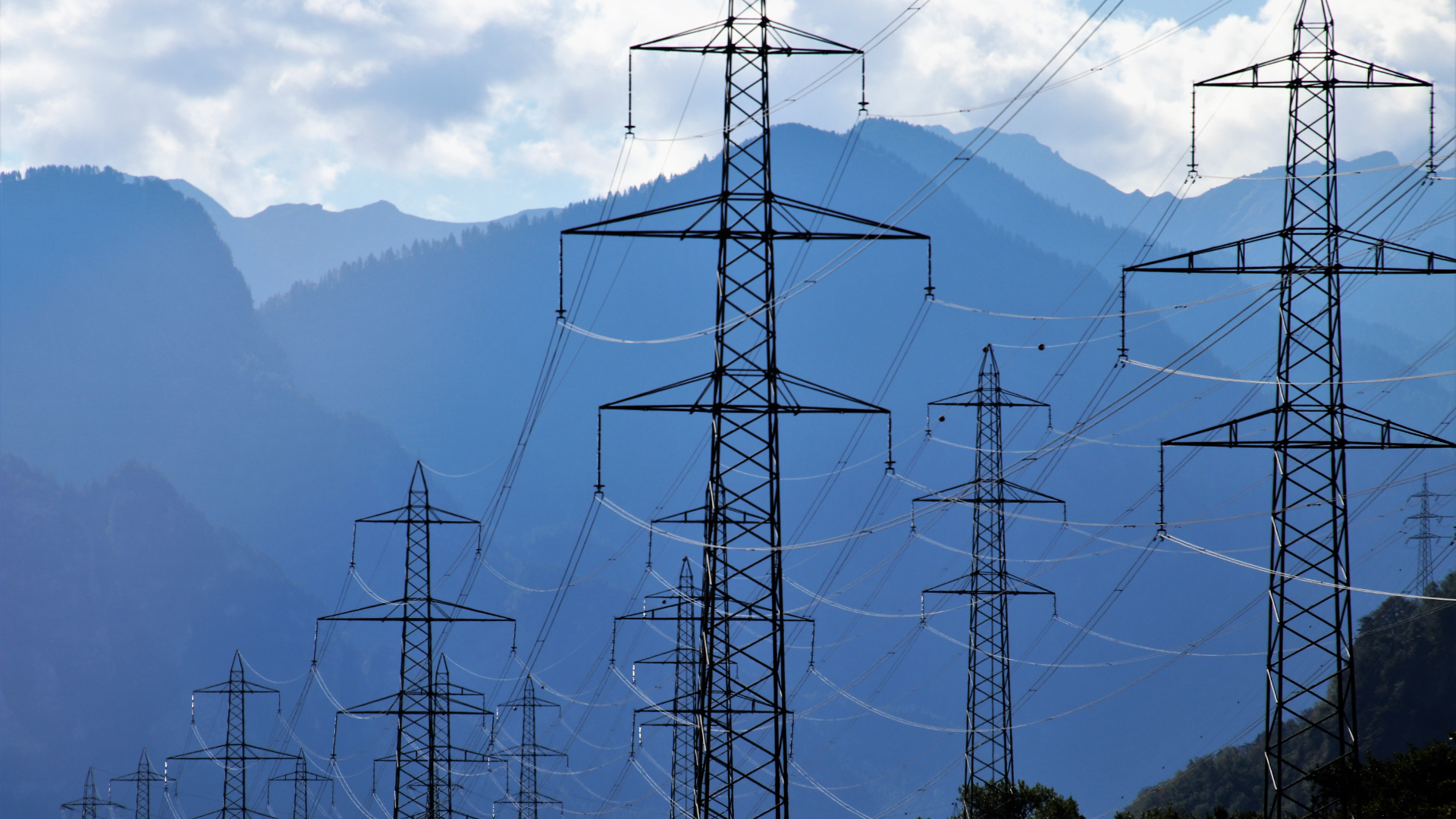 Lignes électriques haute tension et pylônes métalliques devant un paysage de montagne