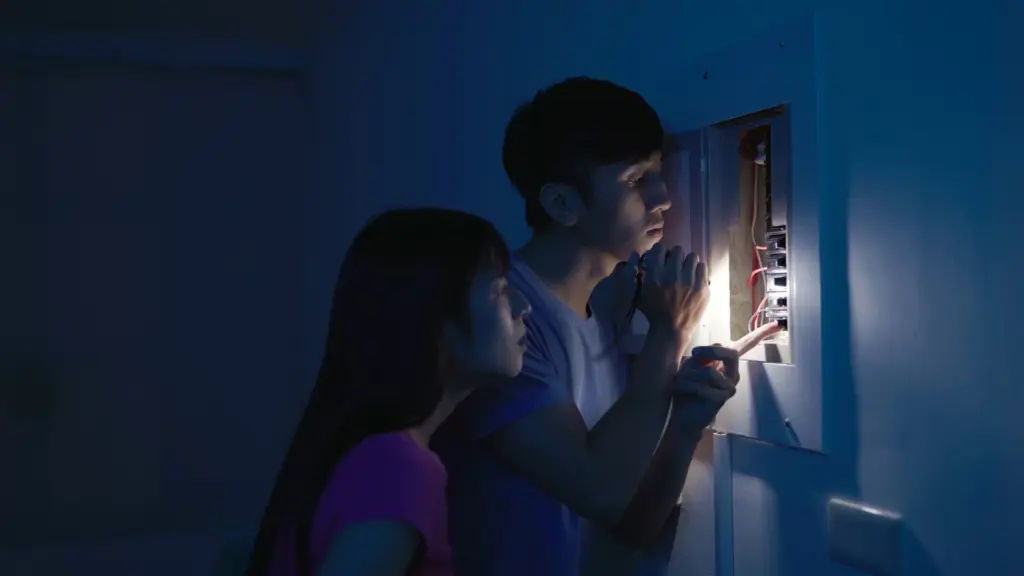 Deux personnes éclairent un tableau électrique à la lampe de poche pendant une coupure de courant